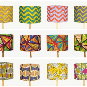 May include: Twelve different lampshades featuring a variety of colourful geometric patterns. The lampshades are all cylindrical and have a wooden base.