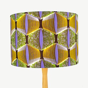 May include: A lampshade with a geometric pattern in shades of yellow, green, purple, and brown. The lampshade is made of fabric and has a cylindrical shape.