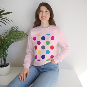 May include: A pink sweatshirt featuring a colourful polka dot pattern. The dots are in various colours, including red, yellow, blue, green, and purple. The sweatshirt has long sleeves and a crew neck.