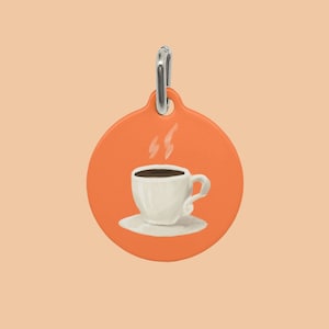 Peut inclure: Breloque orange avec un motif de tasse à café et soucoupe blanche. La tasse contient un liquide brun et de la vapeur s'en échappe.
