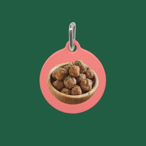 May include: A pink round tag with a silver ring. The tag has a picture of a bowl of brown meatballs.