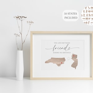 May include: A framed print with a woodgrain background featuring the states of North Carolina and New Jersey with red hearts and a dotted line connecting them. The text reads "The love between friends knows no distance".