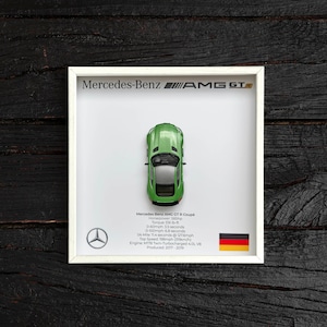 Könnte beinhalten: Ein grünes Modellfahrzeug Mercedes-Benz AMG GT R Coupé in einem weißen Rahmen mit einer schwarz-goldenen deutschen Flagge. Der Rahmen enthält die technischen Daten des Fahrzeugs: Leistung: 585 PS, Drehmoment: 516 lb-ft, 0-60 mph: 3,5 Sekunden, 0-100 mph: 6,8 Sekunden, 1/4 Meile: 11,4 Sekunden bei 127 mph, Höchstgeschwindigkeit: 190 mph (319 km/h), Motor: M178 Twin-Turbocharged 4,0 L V8, Produziert: 2017-2019.