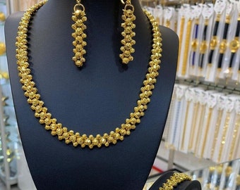 May include: A gold necklace, bracelet, and earrings set. The necklace and bracelet feature a chain of linked, round, textured gold beads. The earrings are long and dangle, with a similar design to the necklace and bracelet.