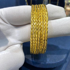 May include: A set of five thin, bright yellow gold bangles, each featuring a repeating chevron or V-shaped textured pattern that catches the light. The bangles are stacked together, displaying a consistent metallic finish and uniform design.