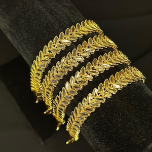 May include: Four gold leaf-shaped bangles stacked on a black velvet display stand.
