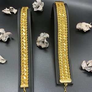 Könnte beinhalten: Zwei goldene Armbänder mit einem Kettenglied-Design. Die Armbänder befinden sich auf schwarzen Präsentationsständern.