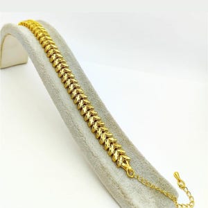 May include: A gold bracelet with a leaf-shaped chain design. The bracelet has a lobster clasp closure.