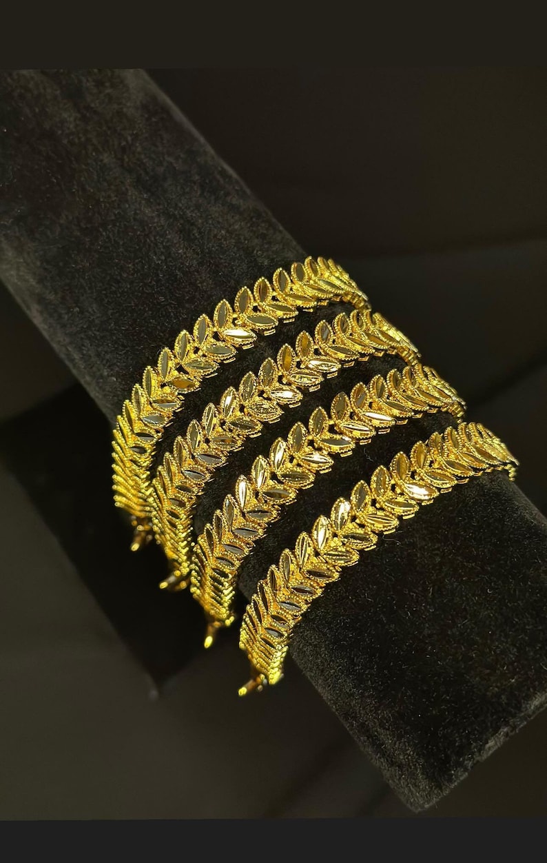 May include: Four gold leaf-shaped bangles stacked on a black velvet display stand.
