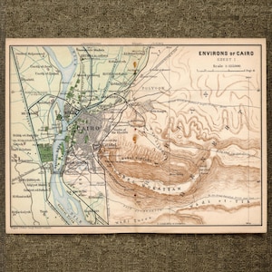 Może przedstawiać: Zabytkowa drukowana mapa zatytułowana Environs of Cairo Sheet 1, przedstawiająca rzekę Nil na niebiesko, obszary miejskie na szaro oraz pustynny teren Gebel Mokattam za pomocą brązowych poziomic. Mapa zawiera czarne etykiety tekstowe i siatkę.
