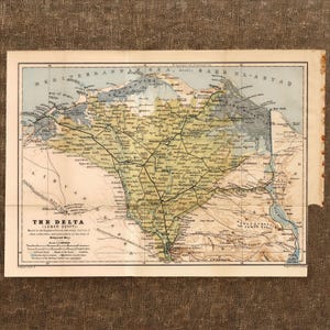 Może przedstawiać: Antyczna papierowa mapa zatytułowana The Delta (Lower Egypt) ze szczegółową kartografią delty Nilu. Mapa wykorzystuje stonowane odcienie zieleni, beżu i błękitu do przedstawienia lądów i wód, z czarnymi etykietami tekstowymi i liniami.