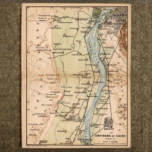 Może przedstawiać: Zabytkowa drukowana mapa zatytułowana Environs of Cairo Sheet II w skali 1:125000. Mapa przedstawia rzekę Nil w kolorze niebieskim, Pustynię Libijską w kolorze beżowym i Pustynię Arabską w kolorze brązowym, z różnymi miastami, piramidami i grobowcami.