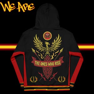 Puede incluir: Sudadera con capucha negra con un diseño de fénix dorado en la espalda, con el texto "THE ONES WHO RISE" en una pancarta roja. Las mangas tienen detalles en rojo. La parte superior de la sudadera tiene el texto "We Are" en amarillo.
