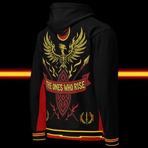 May include: Black hoodie with a gold phoenix design on the back, featuring the text "THE ONES WHO RISE" on a red banner. The hoodie has red side panels and trim with yellow stripes.