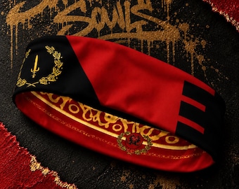 May include: A red and black headband featuring a gold emblem of a sword inside a laurel wreath on the left side, three black horizontal stripes on the right, and a gold patterned interior lining with a circular crest and the text Sovereign Souls.
