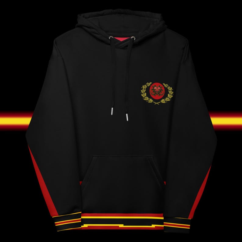May include: Black hooded sweatshirt with red and yellow accents. The sleeves have red stripes, and the cuffs and hem feature red, yellow, and black stripes. A crest with a red emblem and gold laurel wreath is on the chest.