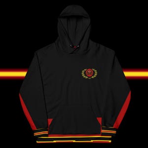 May include: Black hoodie with a hood and a front pocket. The hoodie features red stripes down the sleeves and a red, yellow, and black trim at the bottom. A crest with a red center and gold laurel wreath is embroidered on the chest.