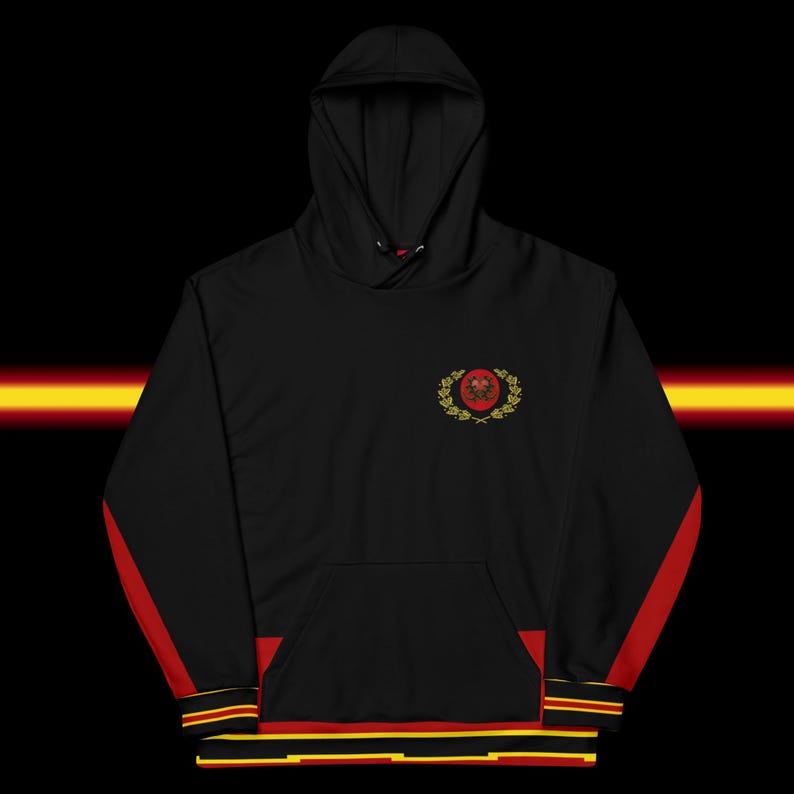 May include: Black hoodie with a hood and a front pocket. The hoodie features red stripes down the sleeves and a red, yellow, and black trim at the bottom. A crest with a red center and gold laurel wreath is embroidered on the chest.