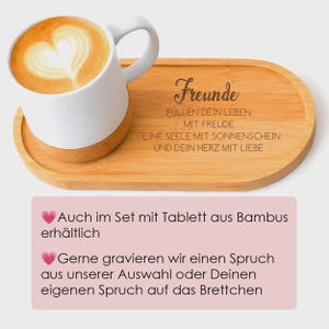 May include: A white ceramic mug with a cork base containing coffee with heart-shaped latte art, resting on an oval bamboo tray engraved with the German text: Freunde, f&uuml;llen dein Leben mit Freude, deine Seele mit Sonnenschein und dein Herz mit Liebe.