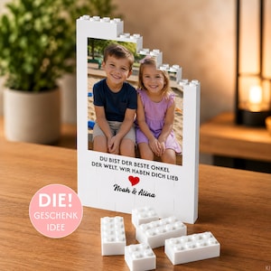 Könnte beinhalten: Ein weißer Baustein-Bilderrahmen mit einem Foto eines Jungen und eines Mädchens. Der Rahmen trägt den Text "DU BIST DER BESTE ONKEL DER WELT. WIR HABEN DICH LIEB" mit einem roten Herz und den Namen "Noah & Alina" unter dem Foto.