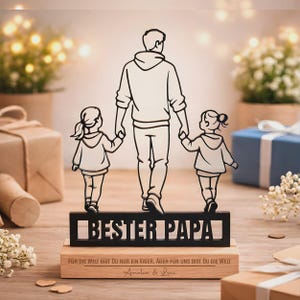 May include: A black silhouette cutout of a parent holding hands with two children, standing on a rectangular wooden base. The cutout features the text "BESTER PAPA" and the base is engraved with "F&Uuml;R DIE WELT BIST DU NUR EIN VATER, ABER F&Uuml;R UNS BIST DU DIE WELT" and "Amalia & Leni".