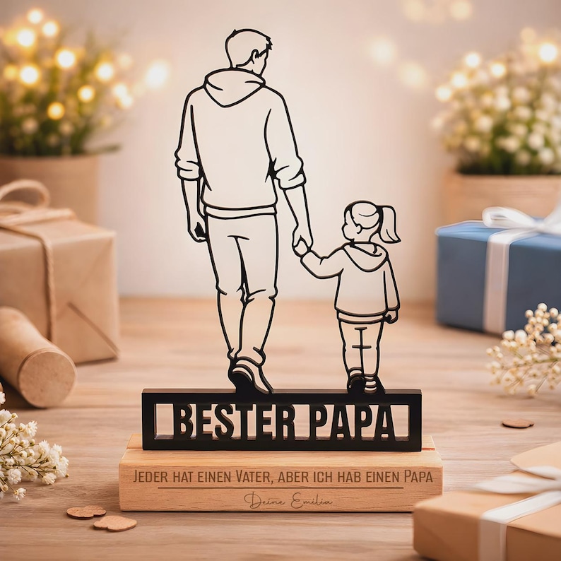 May include: A black metal silhouette of an adult and a child holding hands, mounted on a rectangular wooden base. The metal piece features the text "BESTER PAPA" and the wooden base is engraved with "JEDER HAT EINEN VATER, ABER ICH HAB EINEN PAPA" and "Deine Emilia".