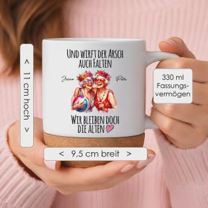May include: A white ceramic mug with a cork base, featuring a graphic of two older individuals with floral crowns and sunglasses, holding a beach ball. The text reads: Und wirft der Arsch auch Falten, wir bleiben doch die Alten. It is 11 cm high, 9.5 cm wide, and holds 330 ml.