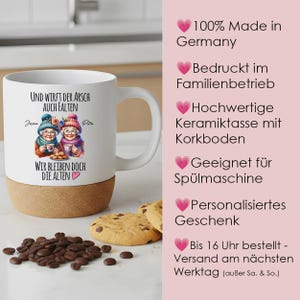 May include: A white ceramic mug with a cork base featuring a graphic of two elderly women in winter hats holding cups, with German text that reads: Und wirft der Arsch auch Falten, wir bleiben doch die Alten. The mug is surrounded by coffee beans and cookies.