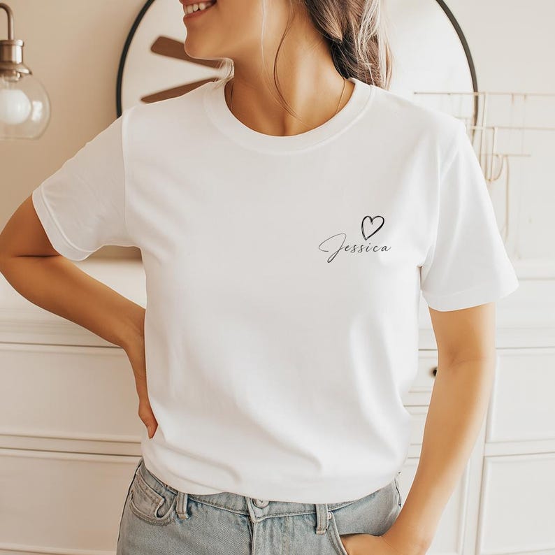 以下が含まれることがあります： クルーネックの白いTシャツ。Tシャツには、筆記体で「Jessica」という名前と小さなハートのシンボルが描かれています。このシャツは柔らかい素材でできており、カジュアルウェアに適しています。