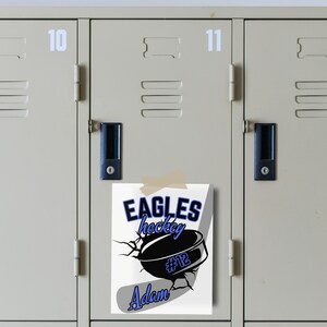 May include: A white poster with a hockey puck and stick design. The text on the poster reads "Eagles hockey #12 Adam". The poster is taped to a gray locker with the number 11 on it.