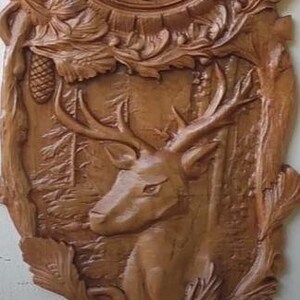 Puede incluir: Reloj de pared de madera con un diseño de ciervo tallado. La esfera del reloj tiene números romanos y detalles de hojas decorativas. Las manecillas del reloj son negras y rojas. El reloj está hecho de madera marrón claro.