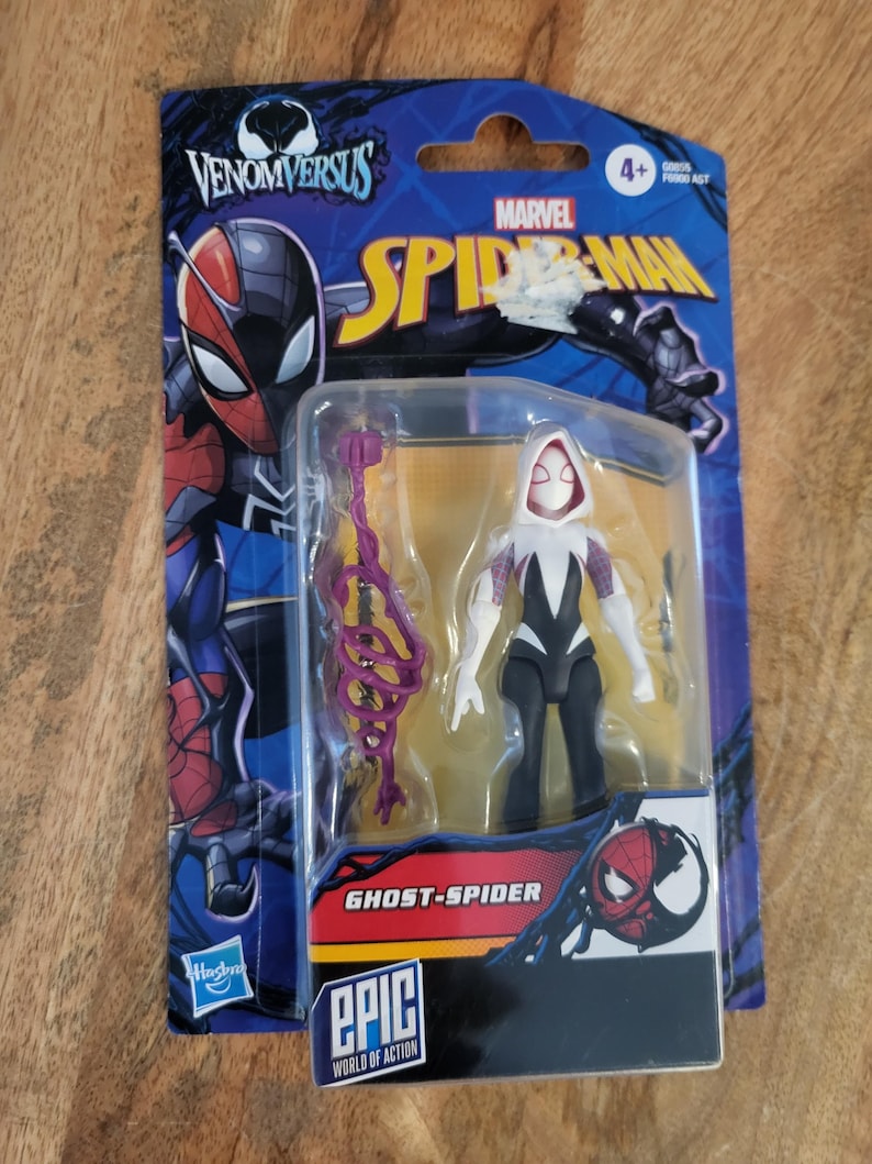 K&ouml;nnte beinhalten: Eine Ghost-Spider-Actionfigur in einer Kunststoffverpackung. Die Figur ist schwarz, wei&szlig; und lila, mit passendem Zubeh&ouml;r. Die Verpackung zeigt das Marvel Spider-Man-Logo und den Text "Venom Versus" und "Epic World of Action".