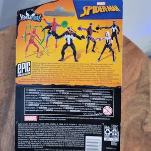 K&ouml;nnte beinhalten: Verpackung f&uuml;r Marvel Spider-Man Actionfiguren, mit verschiedenen Charakteren wie Spider-Man und Venom. Die Verpackung ist &uuml;berwiegend schwarz, blau und gelb, mit den Texten "VENOMVERSUS" und "EPIC WORLD OF ACTION".