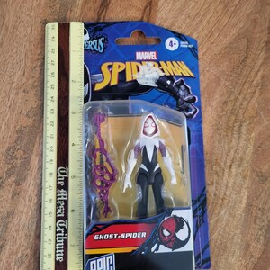 K&ouml;nnte beinhalten: Eine Ghost-Spider-Actionfigur in einer Blisterverpackung. Die Figur ist wei&szlig;, schwarz und lila, mit passendem Zubeh&ouml;r. Die Verpackung zeigt das Marvel Spider-Man-Logo und den Text "Ghost-Spider" und "Epic World of Action."