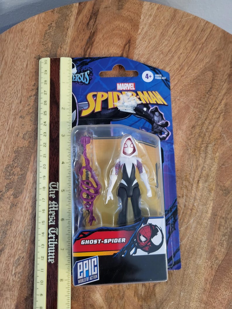 K&ouml;nnte beinhalten: Eine Ghost-Spider-Actionfigur in einer Blisterverpackung. Die Figur ist wei&szlig;, schwarz und lila, mit passendem Zubeh&ouml;r. Die Verpackung zeigt das Marvel Spider-Man-Logo und den Text "Ghost-Spider" und "Epic World of Action."