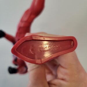 May include: Close-up of the bottom of a red plastic action figure. The figure's foot is visible. The bottom of the figure has the text "HASBRO 54, MADE IN CHINA, &copy;Marvel 2019" printed on it.
