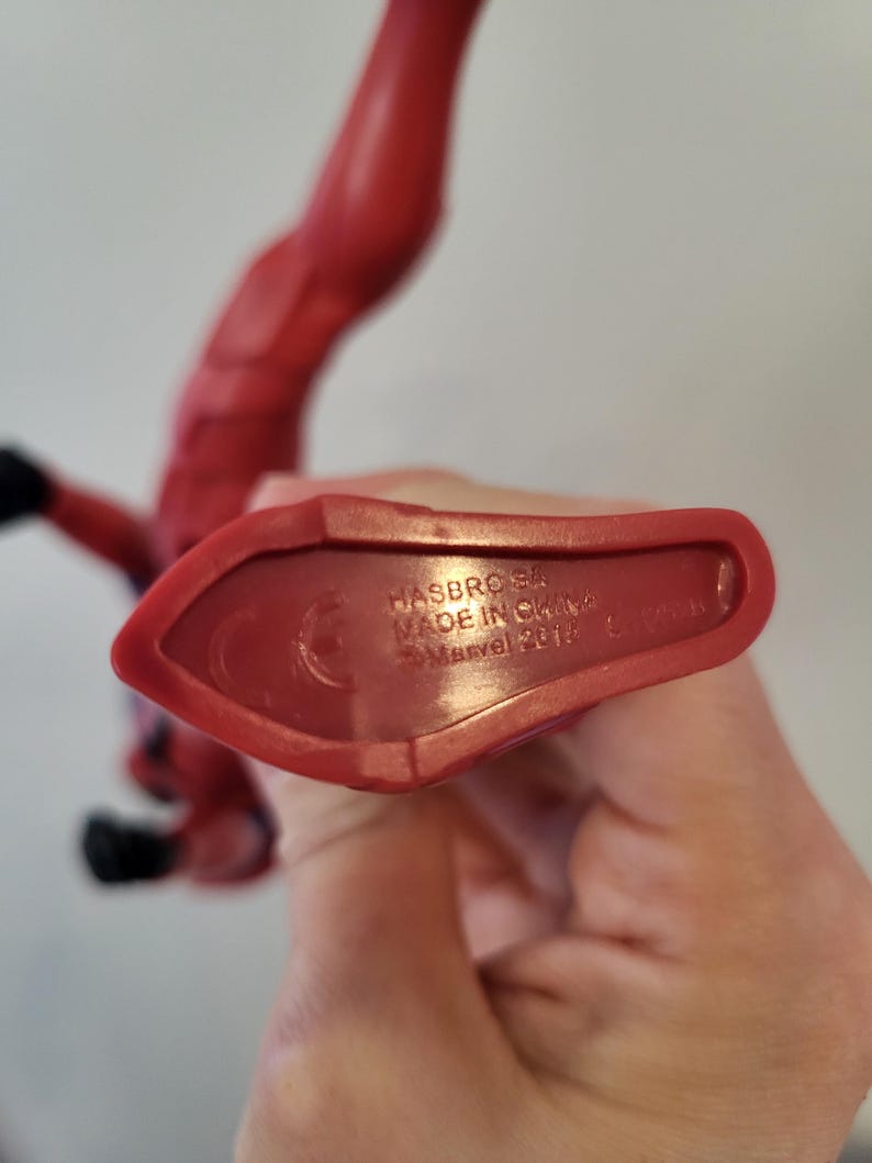 May include: Close-up of the bottom of a red plastic action figure. The figure's foot is visible. The bottom of the figure has the text "HASBRO 54, MADE IN CHINA, &copy;Marvel 2019" printed on it.