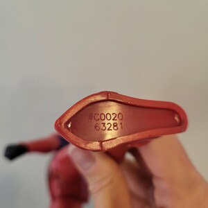 May include: Close-up of the bottom of a red plastic action figure. The figure has a black number "#C0020 63281" printed on the bottom.