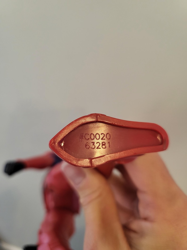 May include: Close-up of the bottom of a red plastic action figure. The figure has a black number "#C0020 63281" printed on the bottom.