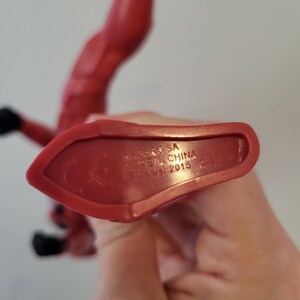 May include: Red plastic action figure with the text "DC Comics" and "Made in China" on the bottom of the foot.