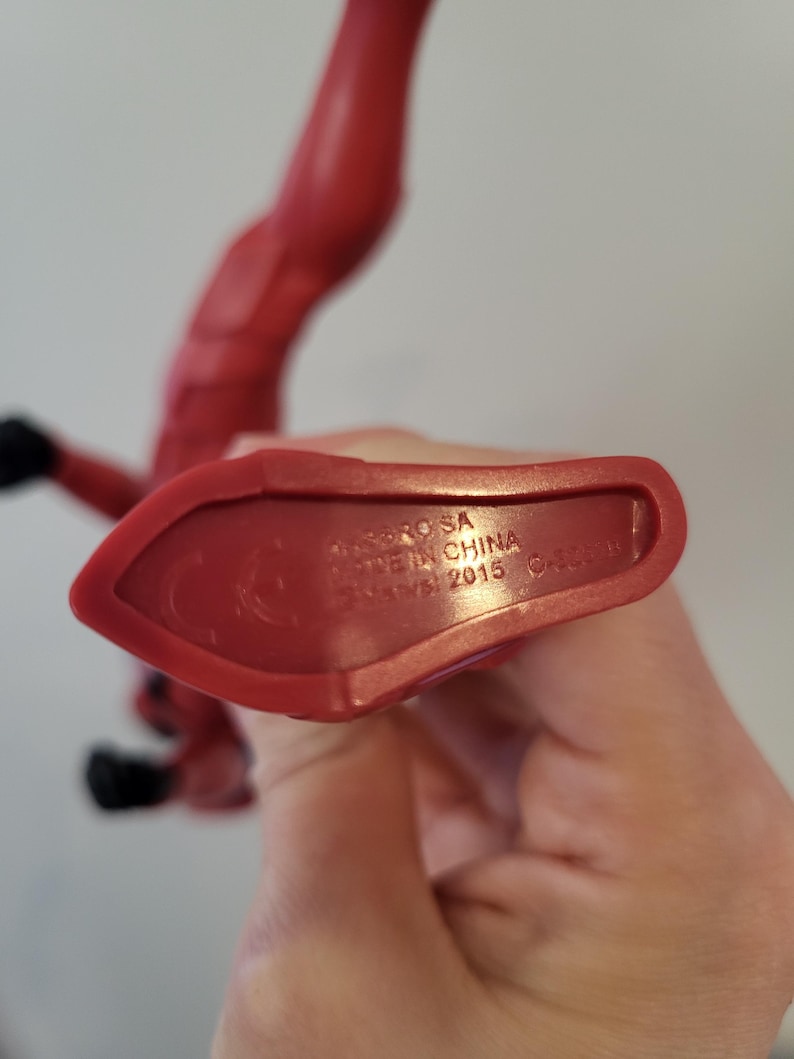 May include: Red plastic action figure with the text "DC Comics" and "Made in China" on the bottom of the foot.