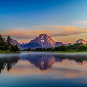 Peut inclure: Une vue panoramique d'une chaîne de montagnes se reflétant dans un lac calme au lever du soleil. Le ciel est d'un bleu vibrant avec des stries de nuages roses et orange. Les sommets des montagnes sont recouverts de neige et le lac est calme et serein.