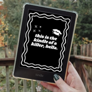 May include: A black Kindle e-reader with a clear protective case displays the text "this is the kindle of a killer, bella." The text is in white, within a white wavy border. The Kindle is held in a hand with a green nail polish.
