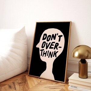 May include: A black and white print with a pink silhouette of a person's head. The text "DON'T OVER-THINK" is written in black inside the head.
