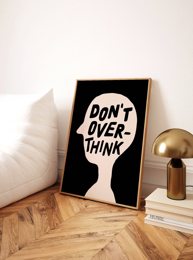 May include: A black and white print with a pink silhouette of a person's head. The text "DON'T OVER-THINK" is written in black inside the head.