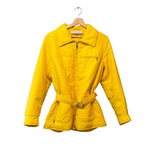 May include: A vibrant yellow jacket with a matching belt and silver buckle. The jacket features a zip-up front, a collar, and a small chest pocket. The brand name "Bogner" is visible on the label.