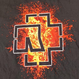 May include: Black t-shirt featuring a white and black graphic of a cross-like symbol with the letters "R" and "W" inside, set against a fiery orange and yellow background. The design has a distressed, grunge aesthetic.