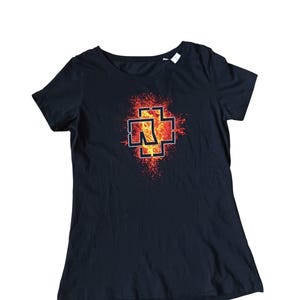 May include: Black crew neck t-shirt featuring a red and orange graphic design. The graphic is a stylized cross with the letter "N" inside, set against a fiery background. The shirt is made of a soft material.