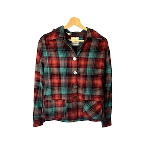 May include: A red, green and black plaid button-up shirt with long sleeves and two pockets. The shirt is hanging on a wooden hanger.