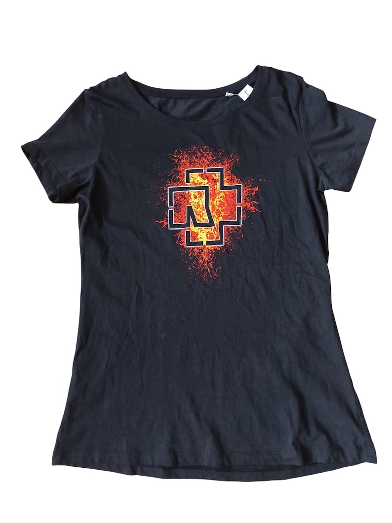May include: Black t-shirt featuring a graphic design with a cross-like symbol in red, orange, and yellow. The design has a fiery, textured appearance. The shirt has a crew neck and short sleeves.